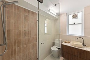 A modern bathroom with a glass shower enclosure, a toilet, and a vanity with a sink. - New Farm Hideaway With Courtyard - 2bed-1bath-1car (Brisbane)