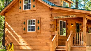 A wooden cabin with a porch, a staircase, and a welcome sign.