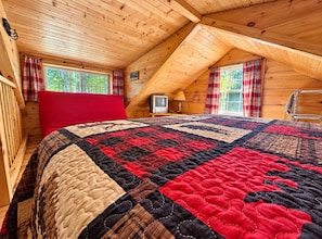 A cozy attic bedroom with a large bed, a television, and a window with plaid curtains. - Hatfield Cabin, Lake Arbutus Beach & Campground Steps Away, Fire Pit, Golf Cart (Merrillan)