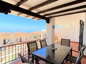 A balcony with a table and chairs, overlooking a coastal area with buildings. - Apartment in Nerja With Sea & Mountain Views (Nerja)