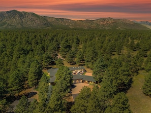 A large, single-story building surrounded by dense forest, with a clear view of the surrounding mountainous landscape. - Luxury Estate with Indoor heated Pool, Spa & Casita (Flagstaff)