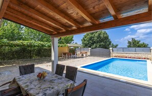 Un'area esterna coperta con piscina, posti a sedere e un barbecue.