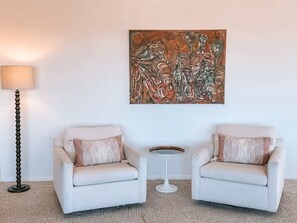 A room with two armchairs, a small round table, a floor lamp, and a large abstract painting on the wall. - Stone & Sky 13-acre desert retreat in Joshua Tree (Yucca Valley)