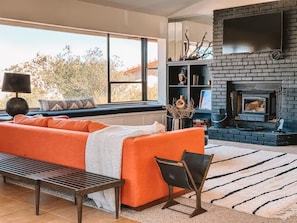 A modern living room with a fireplace, a sofa, a bench, and a bookshelf. - Stone & Sky 13-acre desert retreat in Joshua Tree (Yucca Valley)