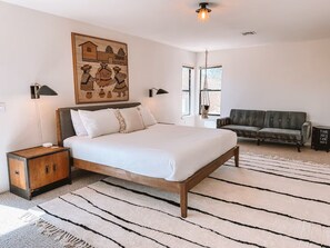 A bedroom with a bed, bedside tables, a hanging light, a sofa, and a large wall painting. - Stone & Sky 13-acre desert retreat in Joshua Tree (Yucca Valley)