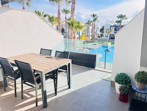 Eine Terrasse mit Holztisch und Stühlen, einer Glasbrüstung, einem Pool und Kübelpflanzen.