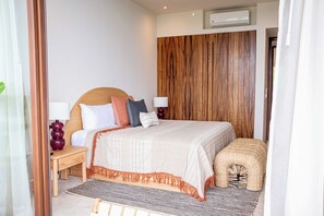 A hotel bedroom with a wooden headboard, a bed with multiple pillows, bedside lamps, a small bench, and a woven basket. - D102 - Two-Bedroom Villa at Cerro del Vigia (Zihuatanejo)