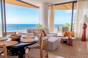 A room with a view of the ocean, a sofa, a dining table with placemats, and a lamp. - D102 - Two-Bedroom Villa at Cerro del Vigia (Zihuatanejo)