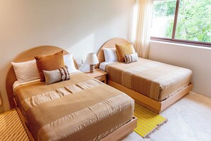 A room with two beds, each with a wooden headboard, a bedside table with a lamp, and a window with a view of greenery. - D102 - Two-Bedroom Villa at Cerro del Vigia (Zihuatanejo)