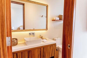 A bathroom with a wooden vanity, a white sink, a mirror, and a toilet. - D102 - Two-Bedroom Villa at Cerro del Vigia (Zihuatanejo)