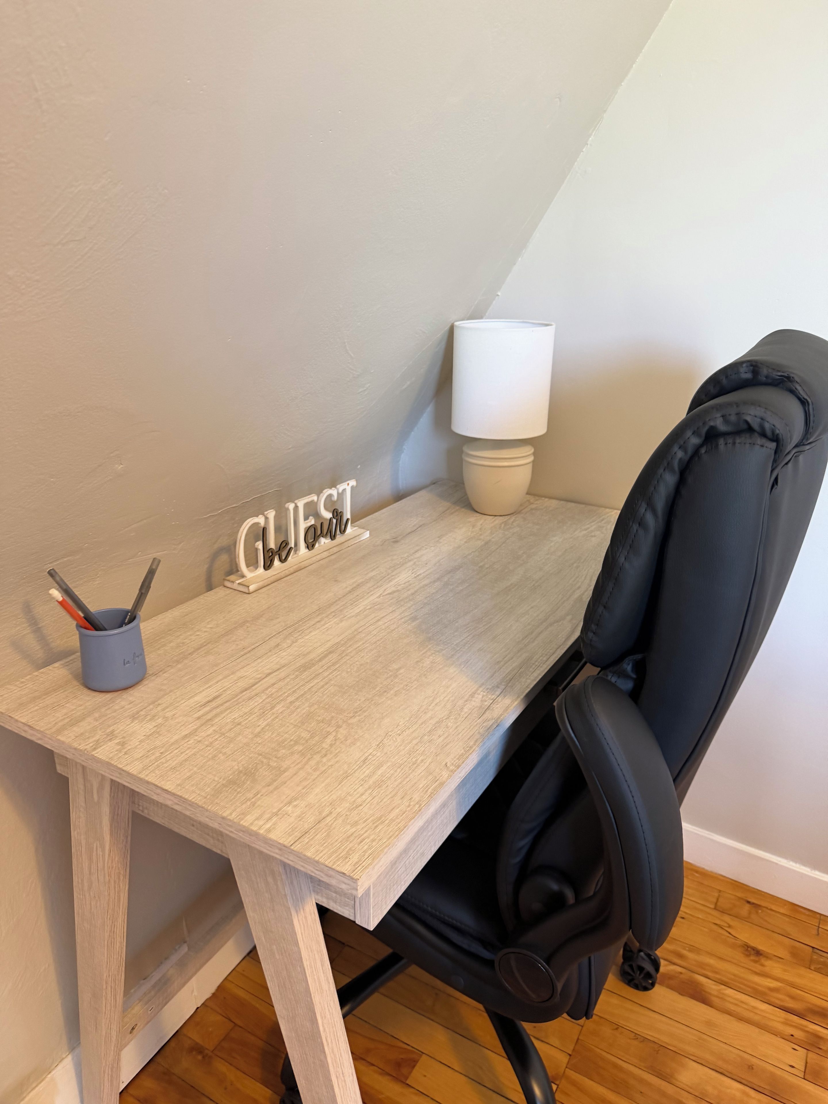 A corner desk with a lamp, a sign reading 'GUEST,' and a cup with writing utensils.