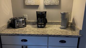 A kitchen with a toaster, a coffee maker, and a trash can on the counter.