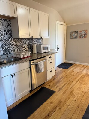 A kitchen with white cabinets, a stainless steel refrigerator, a microwave, and a patterned backsplash.