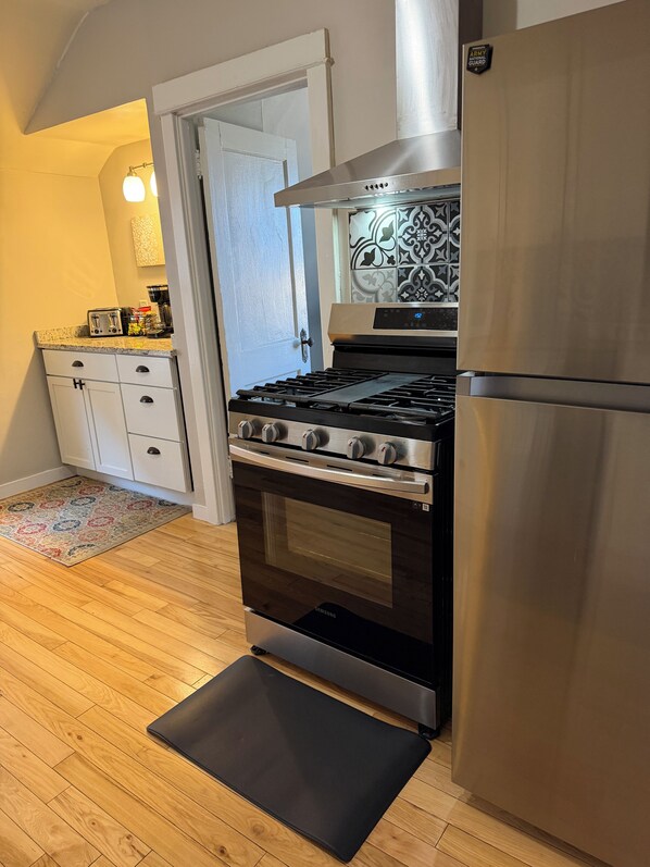 A kitchen with a stainless steel stove, oven, and refrigerator. There is a white door and a patterned rug on the floor.