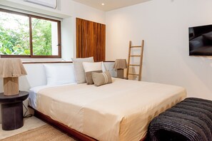 A bedroom with a large bed, a window with curtains, a bedside table with a lamp, a wall-mounted TV, and a wooden ladder. - One-Bedroom Villa at Cerro del Vigia (Zihuatanejo)