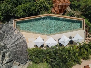 A rectangular pool with clear water, surrounded by a stone wall, and umbrellas for shade. - One-Bedroom Villa at Cerro del Vigia (Zihuatanejo)