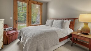 Een slaapkamer met een groot bed, een houten nachtkastje, een nachttafeltje met een lamp, een stoel en een dressoir.