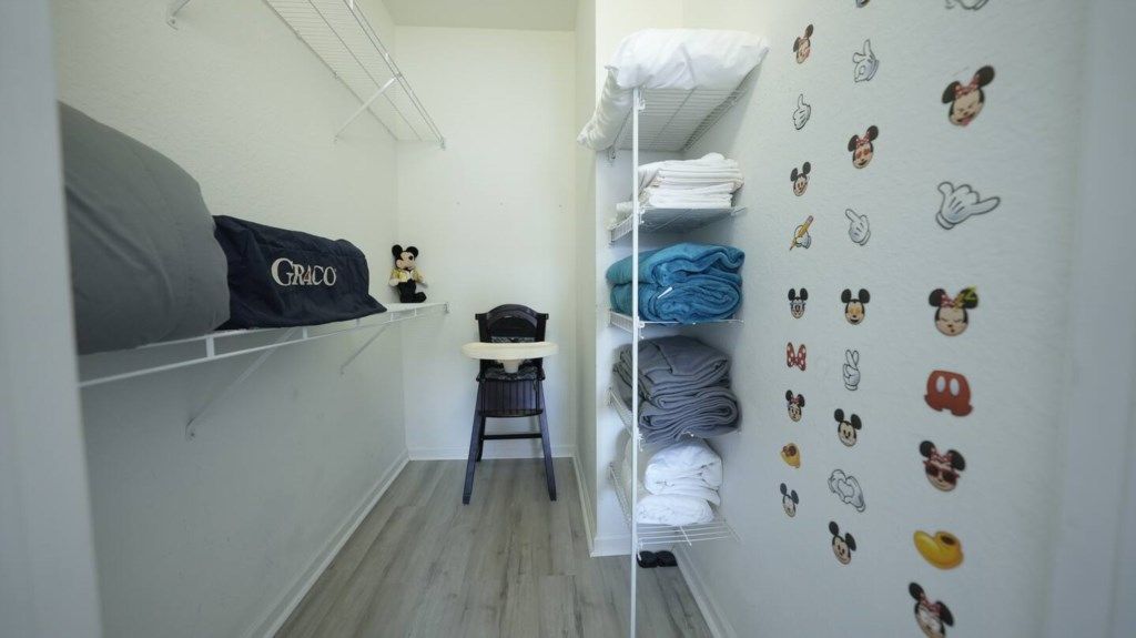 A hotel room with a bed, a chair, a shelf with folded clothes, and a wall with cartoon character stickers.