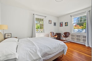Een slaapkamer met een groot bed, twee stoelen, een radiator en wanddecoraties in lijsten.