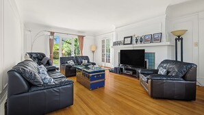 Een woonkamer met leren banken, een blauwe koffer, een flatscreen-tv en een open haard.