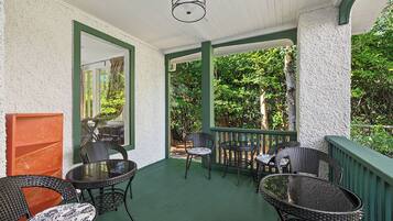 A covered outdoor area with wicker furniture, a glass table, and a view of greenery.