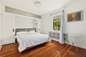 Een slaapkamer met een bed, een raam met gordijnen, een radiator en een klein tafeltje.