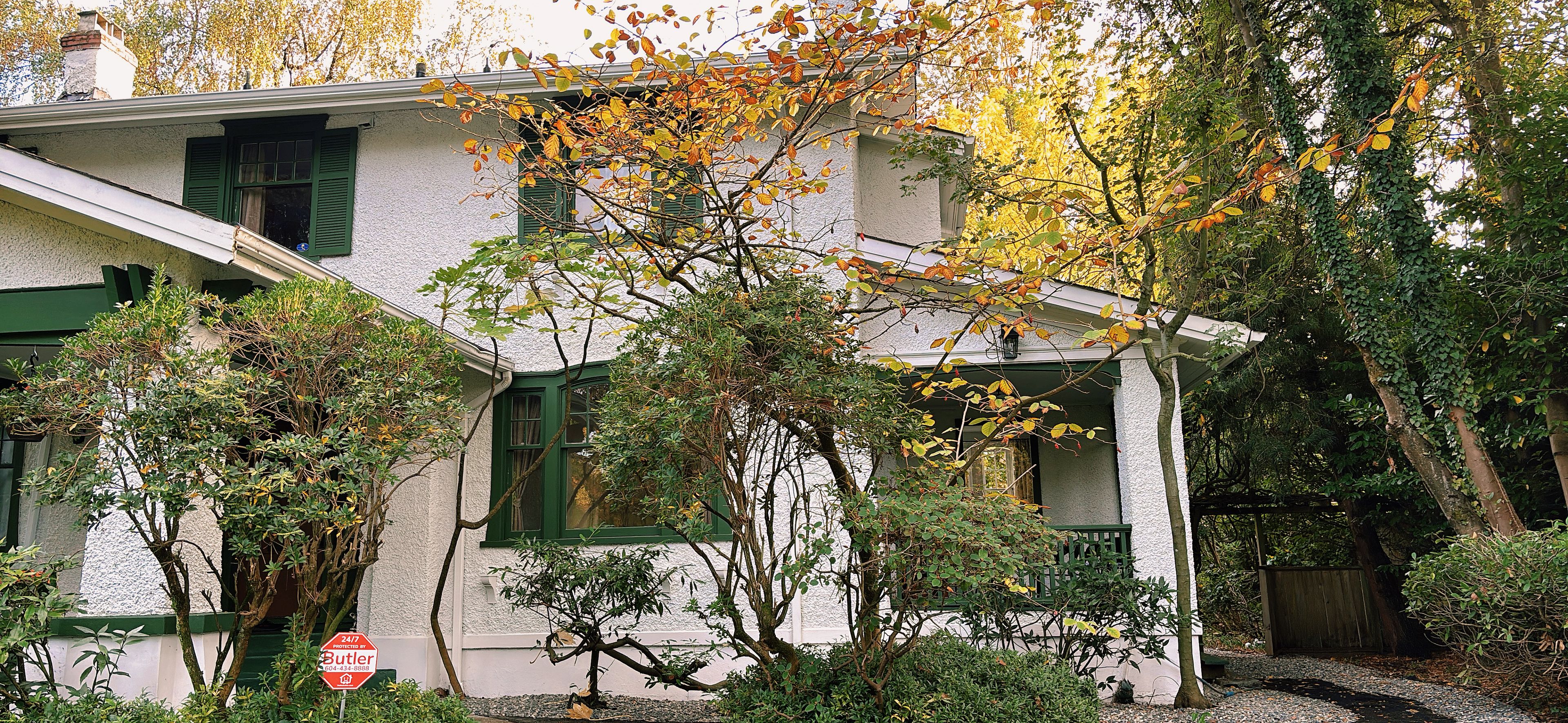A house with a white exterior, green shutters, and a well-maintained garden with various shrubs and trees.