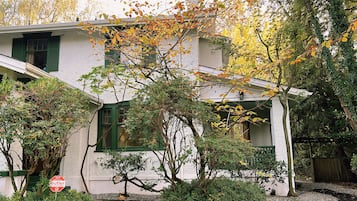 A house with a white exterior, green shutters, and a well-maintained garden with various shrubs and trees.