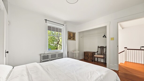 Een slaapkamer met een groot bed, een raam met uitzicht op groen, een klein tafeltje en een stoel.