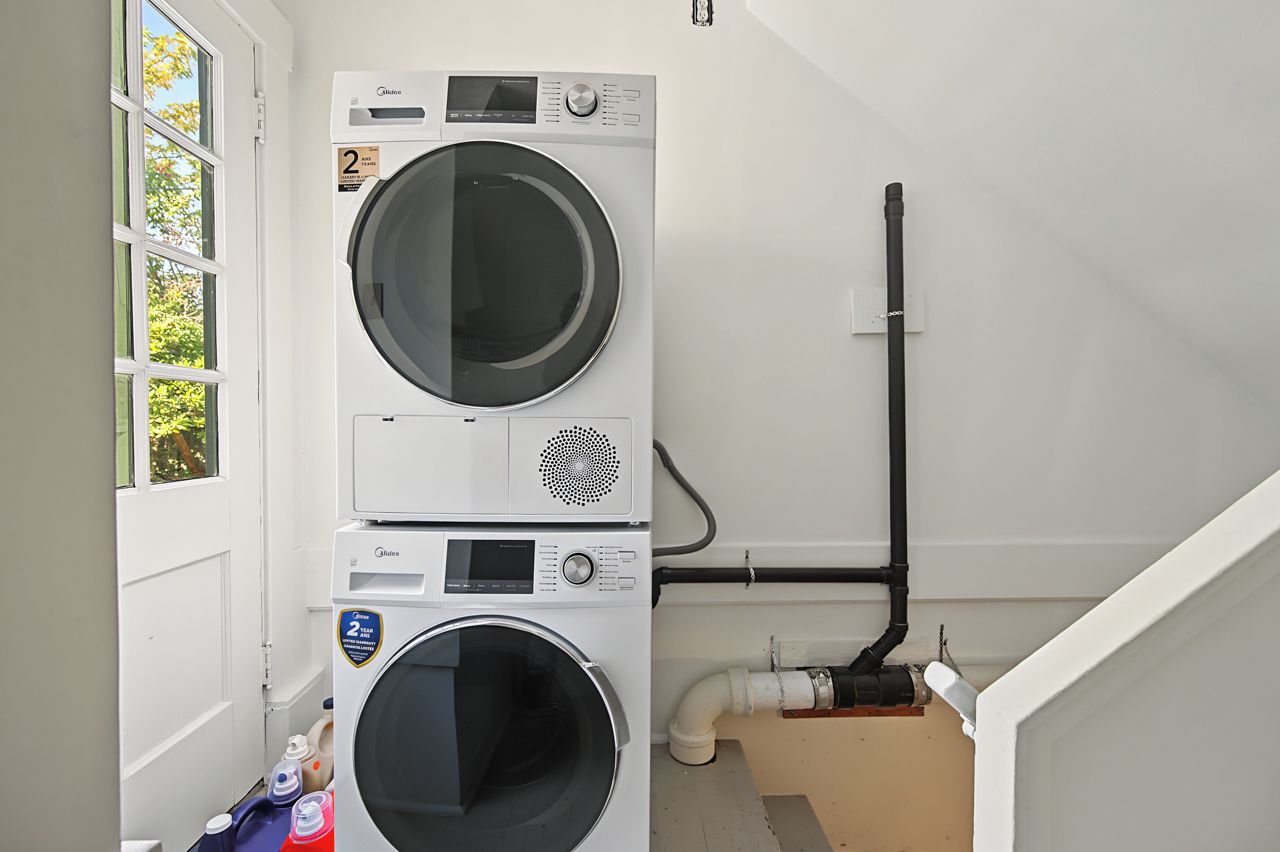 A laundry room with two stacked washing machines, a window, and a visible plumbing system.