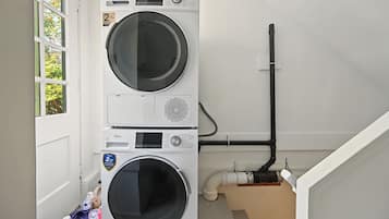 A laundry room with two stacked washing machines, a window, and a visible plumbing system.