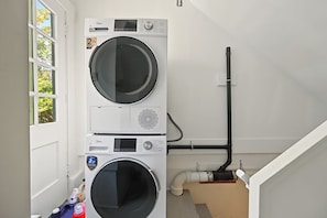 A laundry room with two stacked washing machines, a window, and a visible plumbing system. - Shaughnessy Classic Private Room (Vancouver)