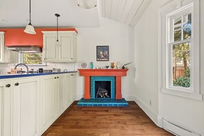 Una cocina con armarios blancos, encimera azul, chimenea roja y ventana con vista a zonas verdes.