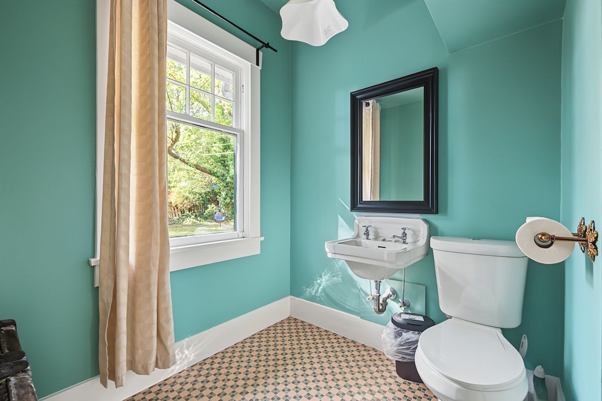 Een badkamer met een raam, een wastafel, een toilet en een spiegel.