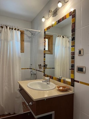 A bathroom with a white sink, a mirror with a colorful frame, and a shower curtain.