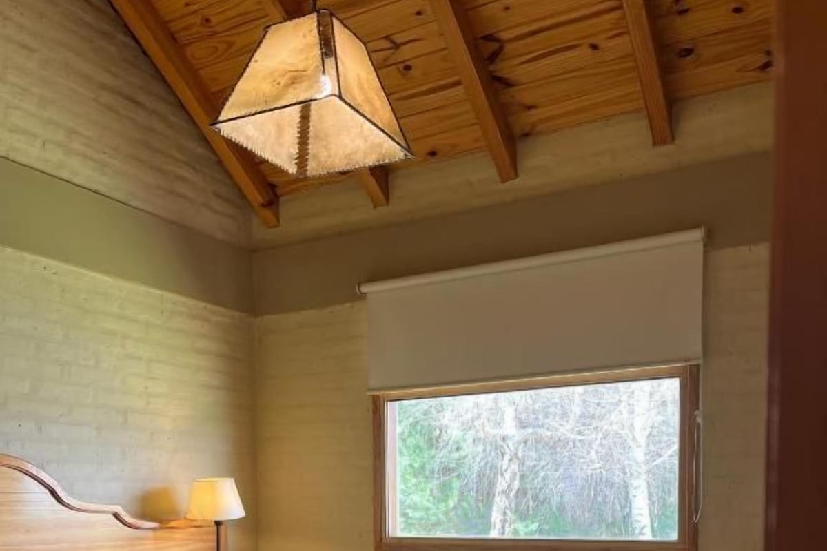 A bedroom with a bed, a window, a lamp, and a bench.