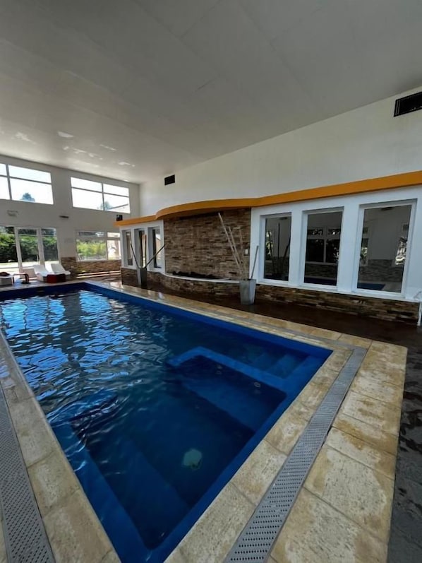 An indoor swimming pool with a clear view of the surrounding area, including a stone wall and windows.