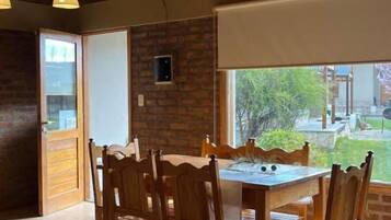 Un comedor con mesa y sillas de madera, pared de ladrillo y ventana con vistas al exterior.