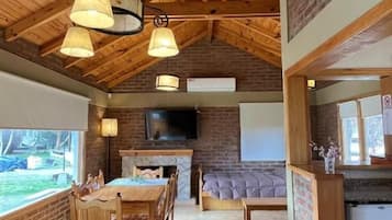 Une pièce spacieuse avec un haut plafond en bois, une cheminée, un coin repas et une cuisine.