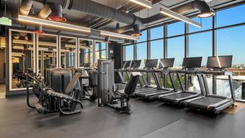 Ein Fitnessstudio mit Laufbändern, Krafttrainingsgeräten und großen Fenstern.