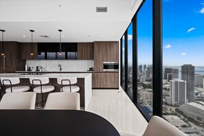 A modern kitchen with a bar area, large windows with a city view, and a dining space with chairs. - Luxury Sky Penthouse Panoramic Views Rooftop Pool (Miami)