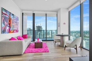 A modern living room with a large window, a pink rug, and a colorful artwork on the wall. - E11EVEN 48th Floor Residence with City Views (Miami)