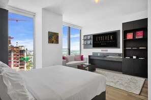 A modern hotel room with a large bed, a sofa, a desk, and a television. There is a view of the city through the windows. - E11EVEN 32nd Floor Studio with Skyline Views (Miami)