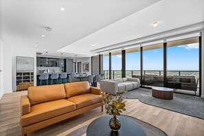Een moderne woonkamer met een leren bank, een eethoek met stoelen, een salontafel en een groot raam met uitzicht op de stad.