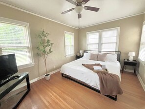 A bedroom with a bed, a television, a ceiling fan, and a potted plant.