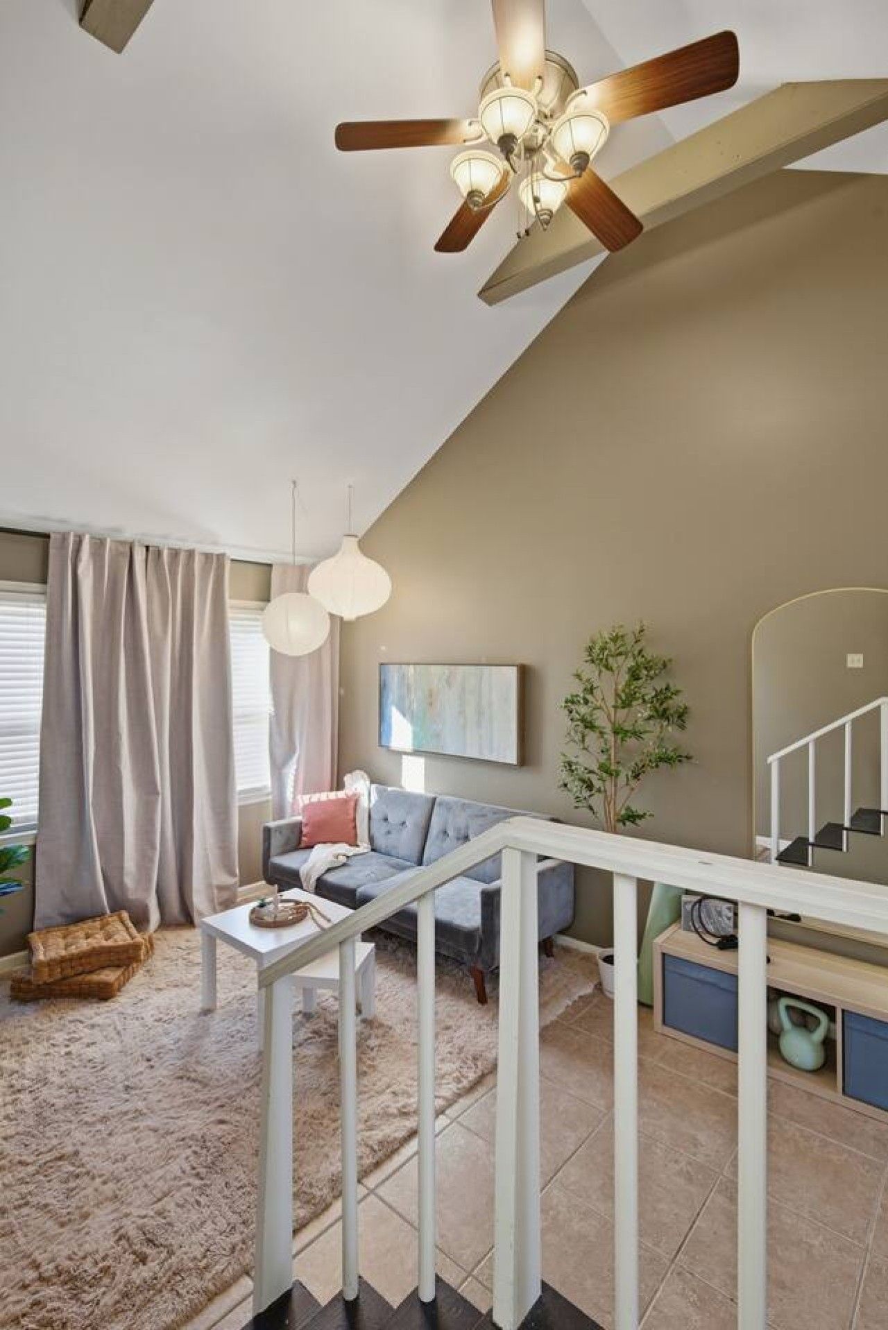 A modern living room with a ceiling fan, a sofa, a coffee table, and a staircase.