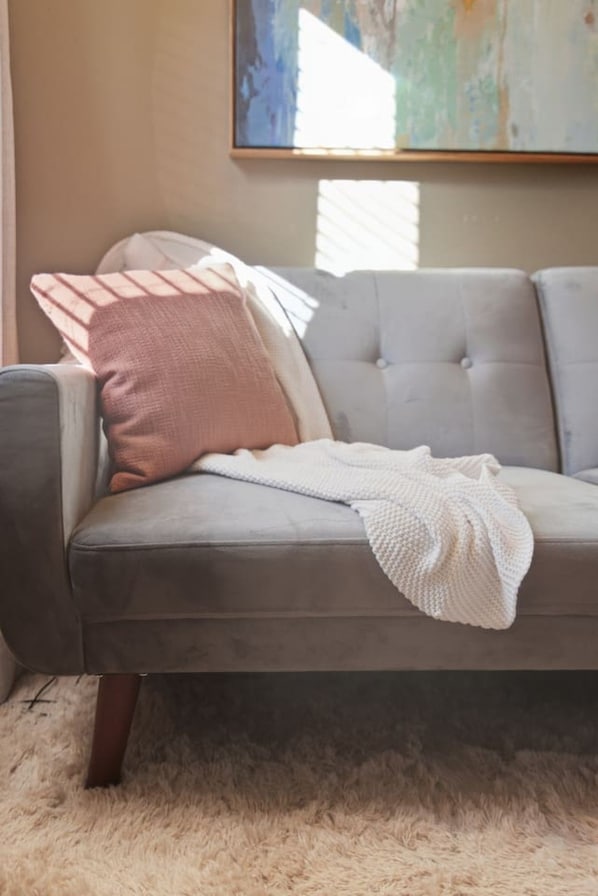 A grey sofa with a white knitted throw, a pink pillow, and a white pillow.