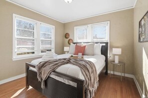 Quarto com uma cama, duas mesas de cabeceira, uma janela com persianas e uma luminária na parede.
