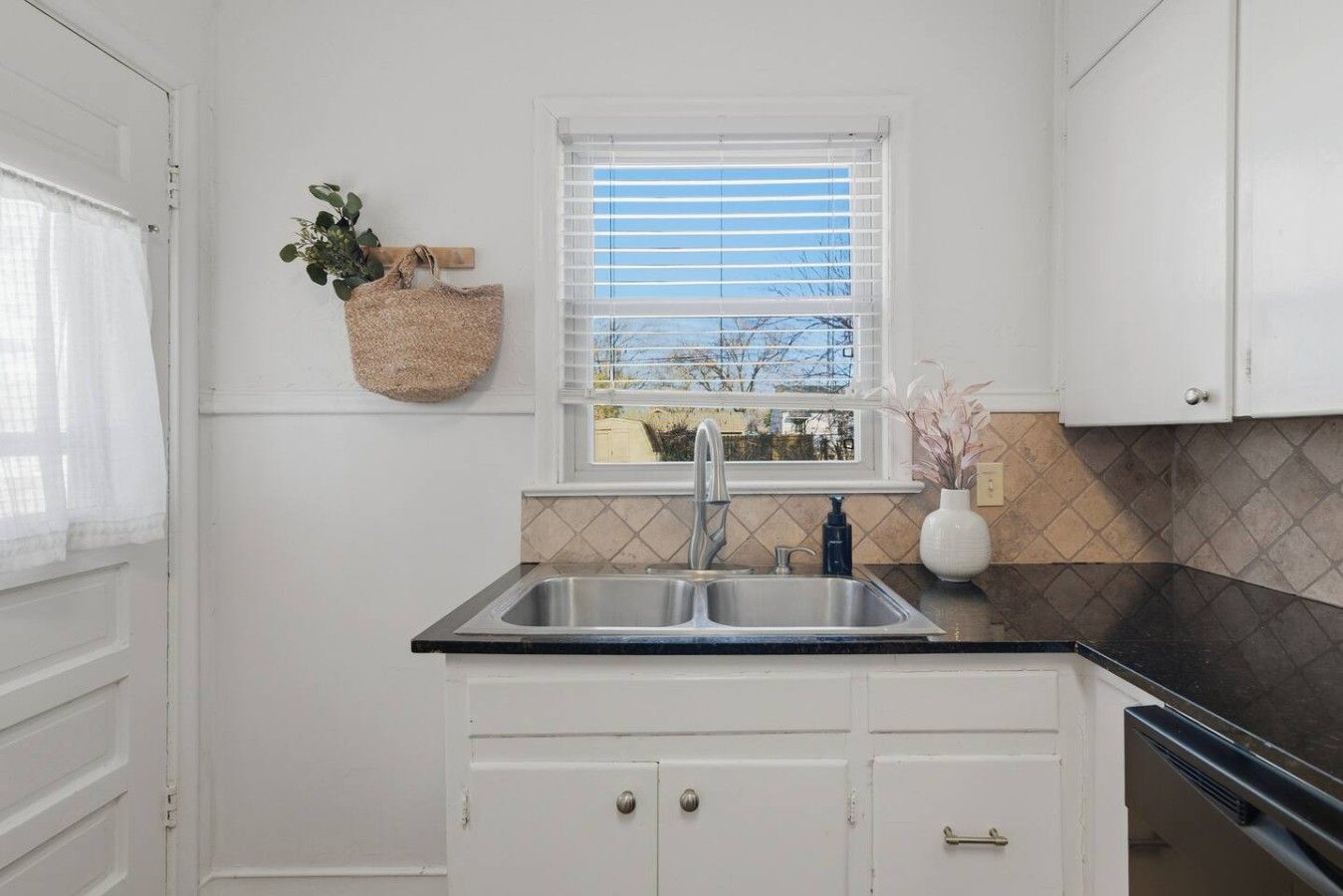 A kitchen with a window, white cabinets, a sink, and a countertop.