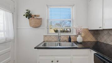 A kitchen with a window, white cabinets, a sink, and a countertop.